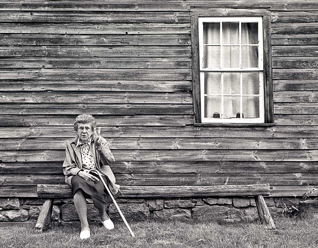 Retired woman sitting outside old wooden house