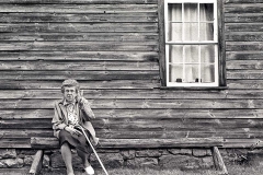 Retired woman sitting outside old wooden house