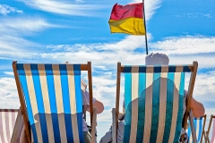 Two people sitting in deck chairs relaxing on the ocean beach in Brighton, England.