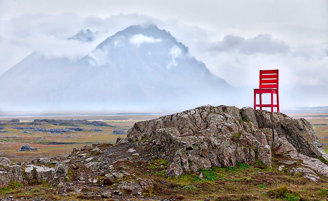 Red chair on rocks in front of mountains and clouds, Iceland.
