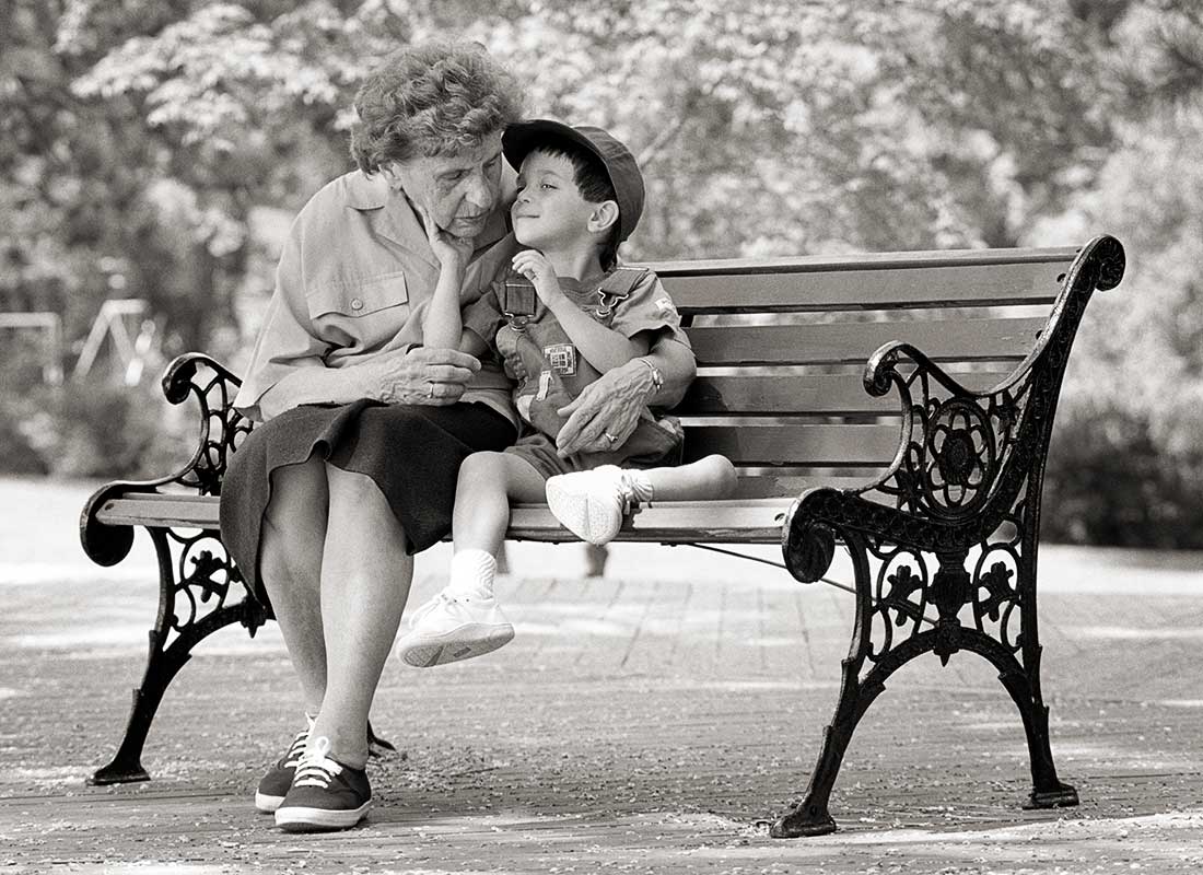 A grandmother hugs her grandson on a park bench.
