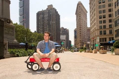 Young man sitting in child's wagon.