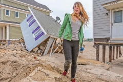 Young woman standing by hurricane damaged home.