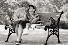 A grandmother hugs her grandson on a park bench.