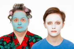 A middle aged woman and a female teenager has curlers in their hair and has a beauty face mask on their faces.